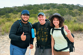 Three people wearing backpacks and hiking through Texas Hill Country